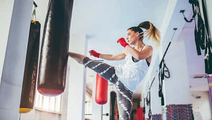 Frau kickt gegen einen Boxsack im Boxstudio