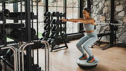 Concentrated woman doing squats on balance board with effort. Interval training in gym.