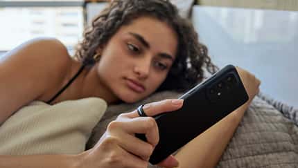 Frau liegt im Bett, blickt auf ihr Smartphone und trägt einen Smart Ring am Finger.