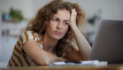 Frau mit lockigen Haaren sitzt nachdenklich vor einem Laptop und stützt den Kopf in die Hand