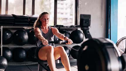 Frau rudert im Fitnessstudio auf einem Ergometer
