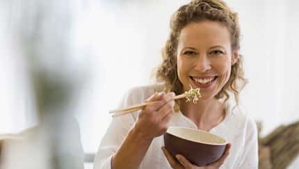 Lächelnde Frau ist ein gesundes Gericht mit Stäbchen aus einer Schale, die sie in der Hand hält