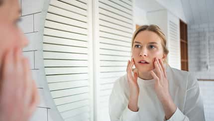 Skin analysis in mirror. Focused woman examines her face for signs of aging and wrinkles in bathroom Skin analysis in mirror. Focused woman examines her face for signs of aging and wrinkles in bathroom