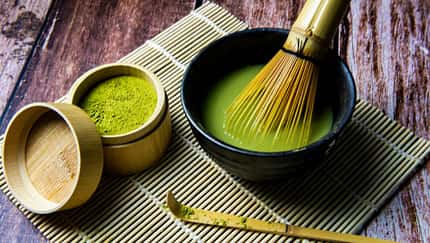 Matcha-Pulver und Matcha-Tee in einer Schale mit Bambusbesen auf einer Bambusmatte.