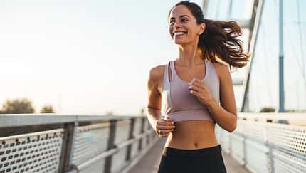 Sportliche Frau joggt lächelnd über eine Brücke