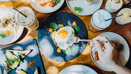 Spiegelei, das auf einem gedeckten Frühstückstisch zwischen weiteren Frühstücksgerichten auf einem Teller liegt.