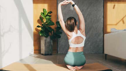 Junge Frau dehnt sich auf einer Yogamatte, indem sie ihre Arme nach oben ausstreckt.