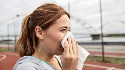 Frau putzt sich beim Sport im Freien die Nase