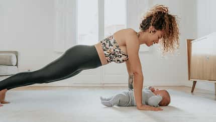 Eine Frau beugt sich lächelnd in Liegestützposition über ihr Baby.