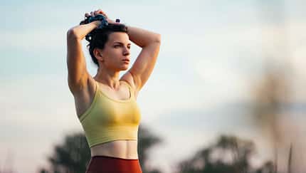 Junge Frau steht mit den Händen über dem Kopf zusammengenommen in der Natur 