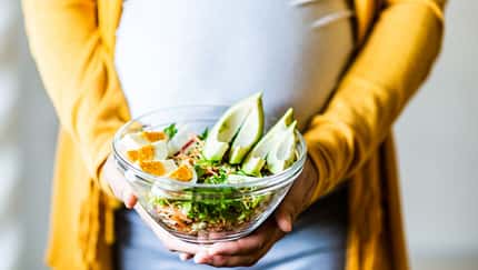 Eine schwangere Frau hält eine Salatschüssel vor dem Bauch