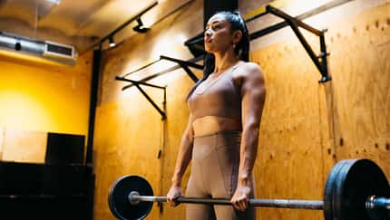 Eine junge Frau hebt im Fitnessstudio eine Langhantel