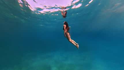 Unterwasseraufnahme einer Frau die elegant taucht und zur Wasseroberfläche hinaufblickt