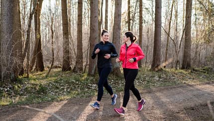 Zwei Frauen gehen in Laufkleidung im Wald und unterhalten sich