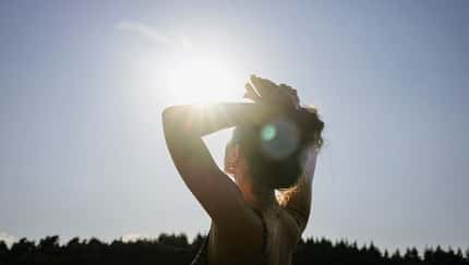 Sonnenlicht fällt in die Kamera, während eine Frau zum Himmel aufblickt