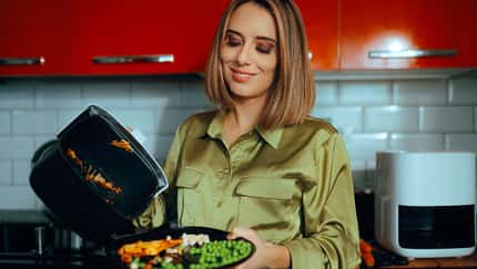Eine Frau schüttet Gemüse aus dem Airfryer auf ihren Teller