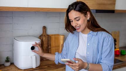 Eine Frau kocht mit dem Airfryer und schaut auf ihr Smartphone
