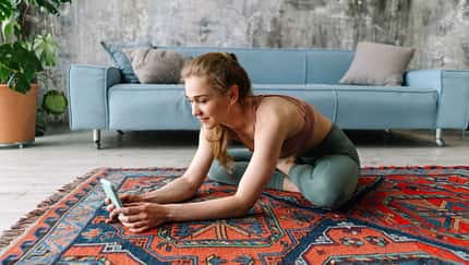 Junge Frau in Sportkleidung sitzt im Wohn-Loft auf dem Boden und schaut auf ihr Smartphone Junge Frau in Sportkleidung sitzt im Wohn-Loft auf dem Boden und schaut auf ihr Smartphone