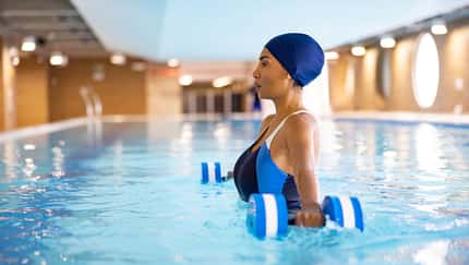 Eine Frau in Badeanzug und Badekappe mit Hanteln beim Aquafitness im Schwimmbad