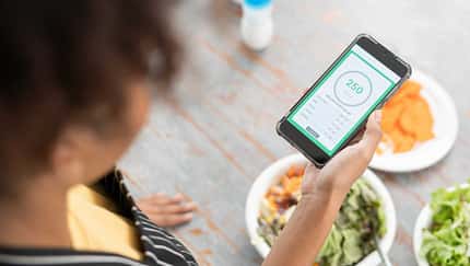 Frau checkt während dem Essen ihre Intervallfasten-App auf dem Smartphone Frau checkt während dem Essen ihre Intervallfasten-App auf dem Smartphone