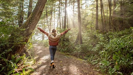 Frau läuft im Wald durch eine Waldlichtung und streckt die Arme zu den Seiten aus Frau läuft im Wald durch eine Waldlichtung und streckt die Arme zu den Seiten aus