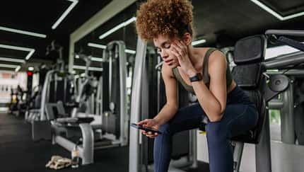 Junge Frau macht eine Pause im Fitnessstudio und schaut auf ihr Smartphone