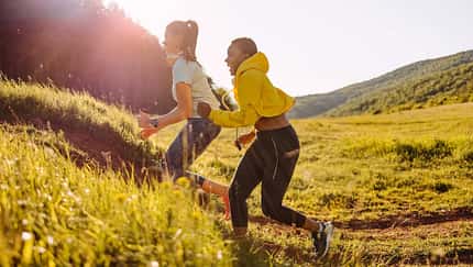 Zwei Freuen joggen durch eine hügelige Landschaft und werden von der Abendsonne angeschienen Zwei Freuen joggen durch eine hügelige Landschaft und werden von der Abendsonne angeschienen