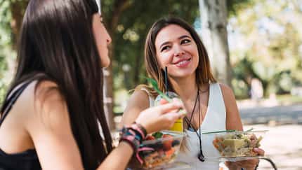 Zwei junge Frauen sitzen im Park und essen Salat Zwei junge Frauen sitzen im Park und essen Salat