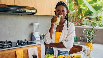 Eine junge Frau steht in ihrer Küche und trinkt einen Smoothie. Eine junge Frau steht in ihrer Küche und trinkt einen Smoothie.