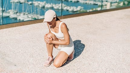 Eine Frau in Sportkleidung fasst sich an ihr Knie beim Outdoor-Training Eine Frau in Sportkleidung fasst sich an ihr Knie beim Outdoor-Training