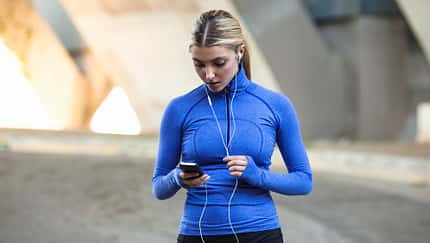 Eine Frau in Sportkleidung schaut beim Laufen auf ihr Smartphone