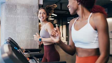 Zwei Sportlerinnen trainieren auf einem Laufband im Fitnessstudio