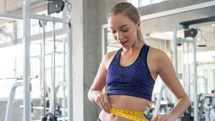 Junge Frau im Fitnessstudio misst ihren Bauchumfang Junge Frau im Fitnessstudio misst ihren Bauchumfang