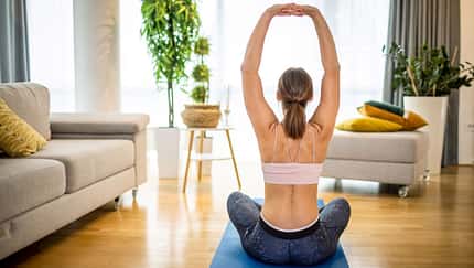 Eine Frau von hinten, wie sie auf einer Yogamatte Übungen für den Rücken praktiziert Eine Frau von hinten, wie sie auf einer Yogamatte Übungen für den Rücken praktiziert