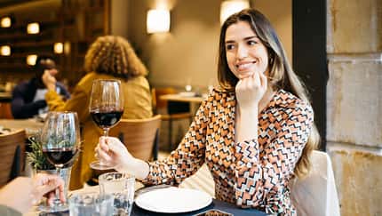 Eine Frau sitzt im Restaurant und trinkt ein Glas Rotwein Eine Frau sitzt im Restaurant und trinkt ein Glas Rotwein
