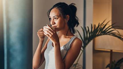 Eine Frau in einem grauen Top schaut aus dem Fenster und hält einen Kaffeebecher in den Händen Eine Frau in einem grauen Top schaut aus dem Fenster und hält einen Kaffeebecher in den Händen