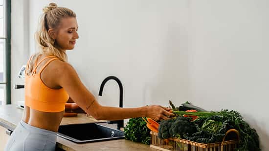 Eine junge Frau in Sportkleidung wäscht Gemüse