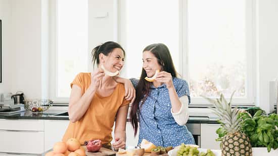 Two happy women in kitchen preparing fruit
