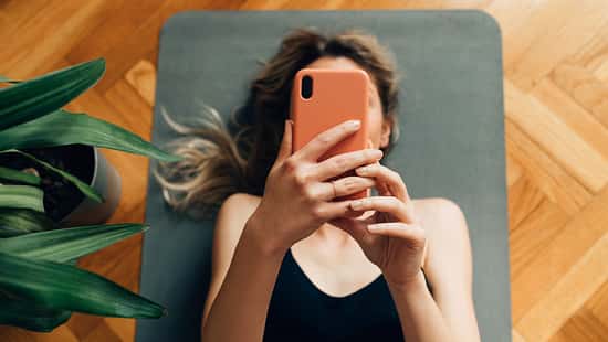 Frau liegt auf Yogamatte und schaut auf ihr Handy