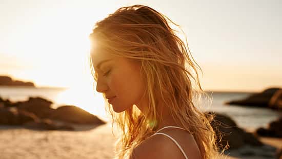 Eine Frau mit blonden Haaren am Strand bei Sonnenuntergang