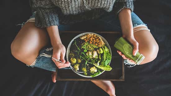 Eine Frau isst vegane Salat Bowl mit einem grünen Smoothie