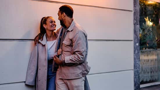 Ein junges Paar spaziert durch eine Stadt, während sich Mann und Frau verliebt angucken