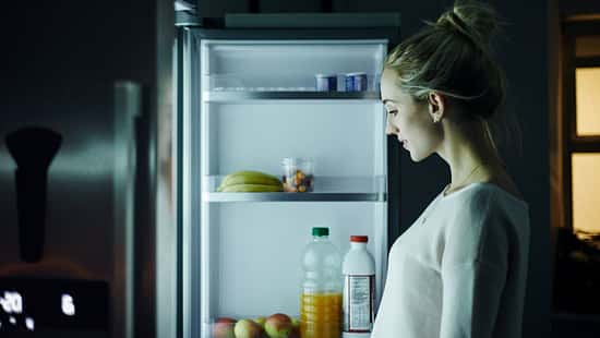 Eine Frau steht nachts vor dem Kühlschrank und schaut, was sie essen möchte