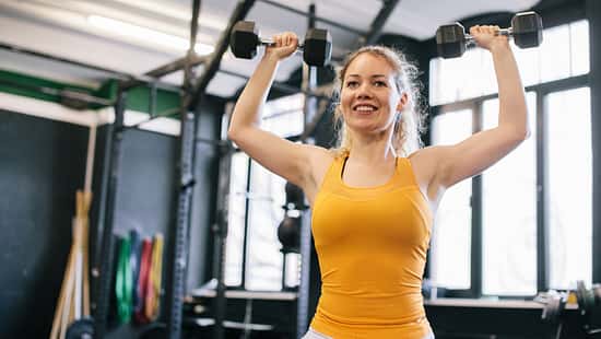 Eine Frau im gelben Oberteil macht Übungen mit Kurzhanteln für die Arme