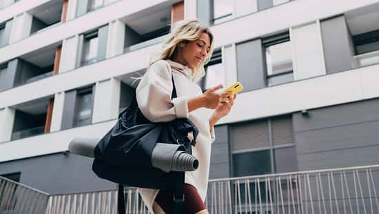 Happy Sporty Woman in a White Sweatshirt Using a Mobile Phone Outdoors