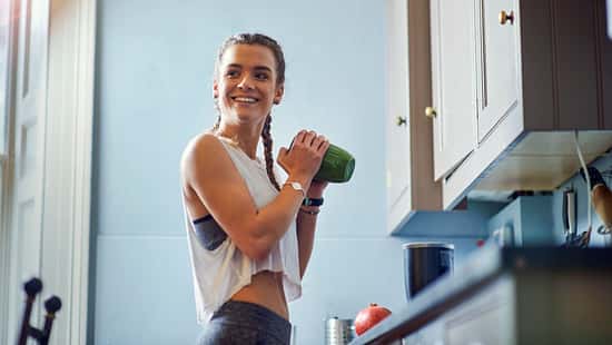 Eine Frau in Sportkleidung mit einem grünen Shaker in der Hand 