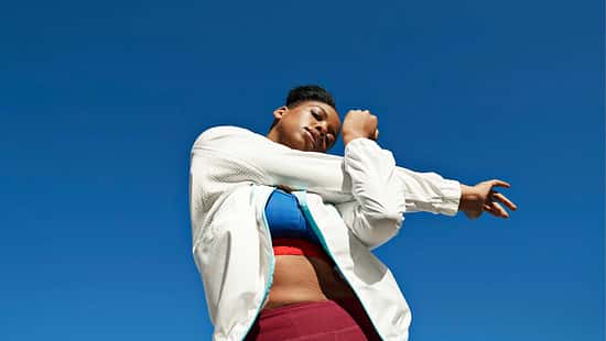 Froschperspektive einer Frau, die ihre Schulter dehnt. Hintergrund nur blauer Himmel