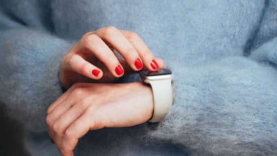 Hände mit rotlackierten Fingernägeln tippen auf Smartwatch