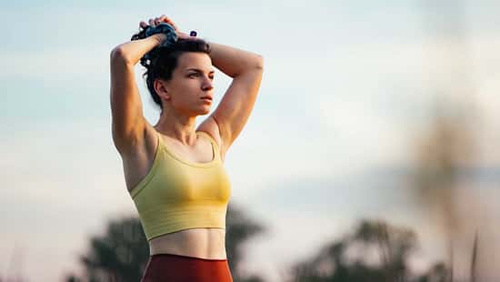 Junge Frau steht mit den Händen über dem Kopf zusammengenommen in der Natur 