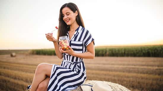 Frau isst Obst und sitzt auf einem Heuballen auf dem Feld